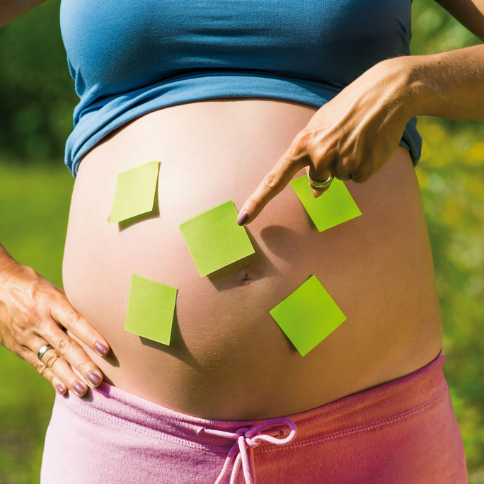 Ein schwangerer Bauch, der mit Postits beklebt ist 