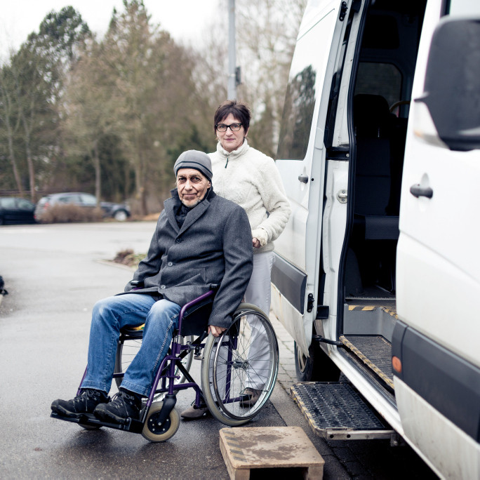 Pflegerin hilft Senior aus einem Bulli in den Rollstuhl