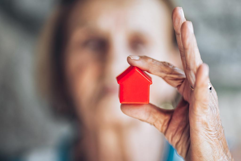 Eine ältere Frau hält ein rotes Holzhaus zwischen den Fingern