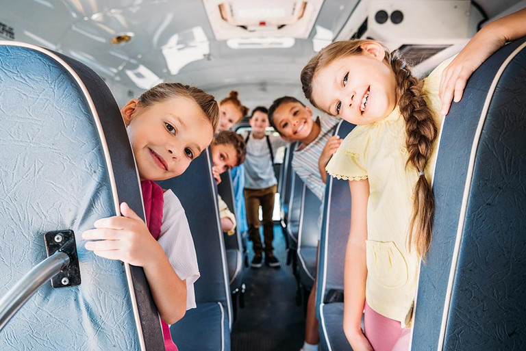 Gruppe von Schulkindern, die mit einem Schulbus fahren und in die Kamera schauen