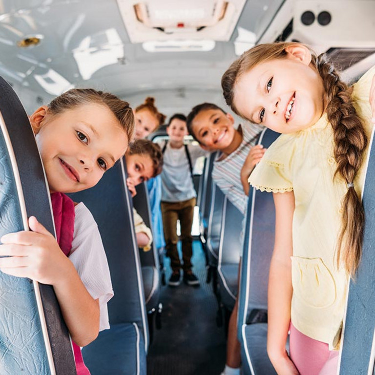 Gruppe von Schulkindern, die mit einem Schulbus fahren und in die Kamera schauen