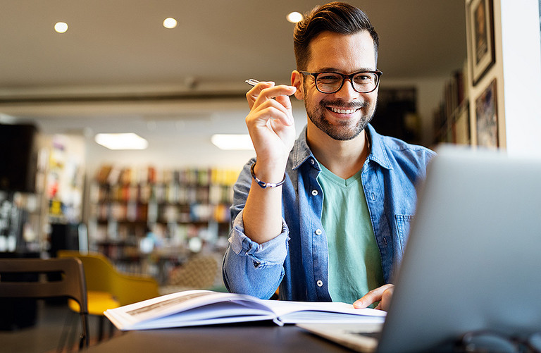 Ein junger Mann arbeitet in einer Bibliothek an seinem Laptop