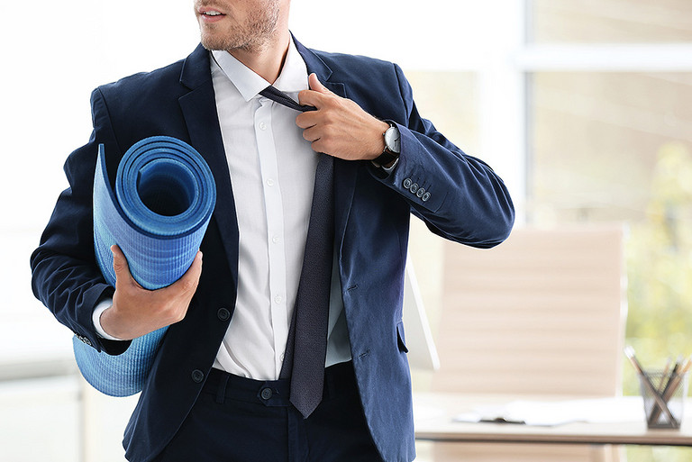 Ein Mann im Anzug trägt eine Gymnastikmatte unter dem Arm