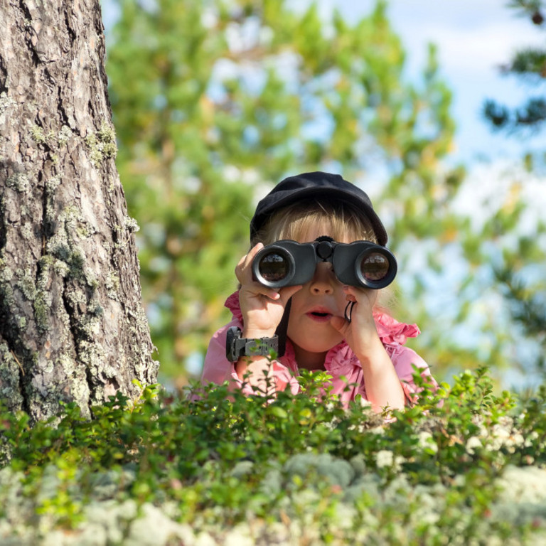 Ein Kind liegt im Gras und schaut durch ein Fernglas