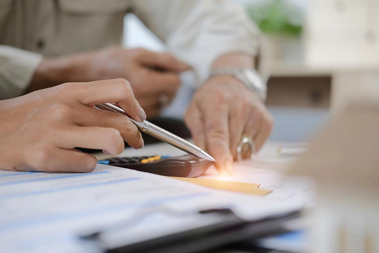 Nahaufnahme von den Händen eines Finanzberaters mit einem Taschenrechner und Unterlagen