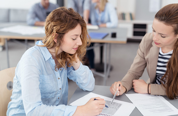 Eine junge Frau erklärt einer Studentin etwas in den Unterlagen