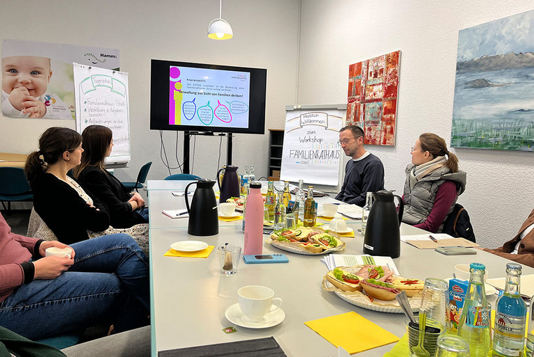 Einige Personen sitzen an einem Tisch und hören einer Präsentation zu.