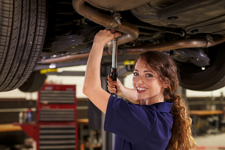 Automechanikerin arbeitet unter einem Auto