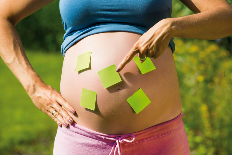 Ein schwangerer Bauch, der mit Postits beklebt ist 