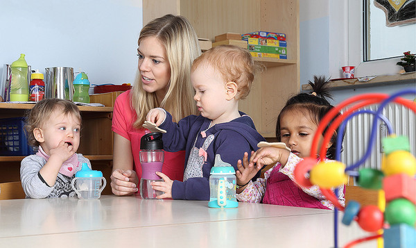 Eine Erzieherin sitzt mit mehreren Kitakindern an einem Tisch