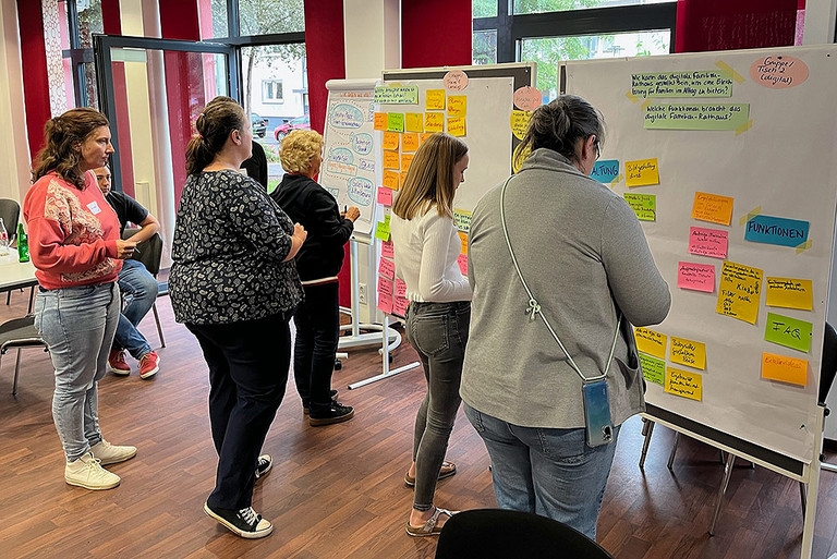 Mehrere Personen kleben in einem Workshop bunte Zettel an eine Pin-Wand 