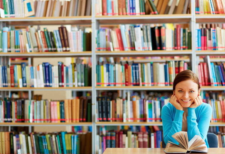 Studentin sitzt in der Bibliothek vor einem aufgeschlagenem Buch