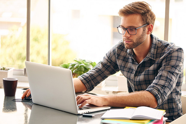 Ein junger Mann sitzt an einem Schreibtisch und arbeitet mit einem Laptop