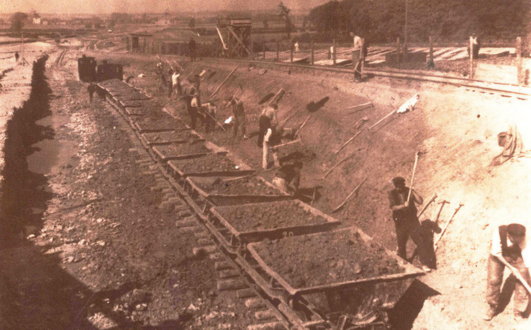 Arbeiter schaufeln Abraum in Eisenbahnloren