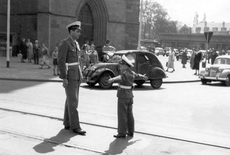 Ein Polizist und ein Junge in Polizeiuniform regeln den Verkehr im Jahre 1955