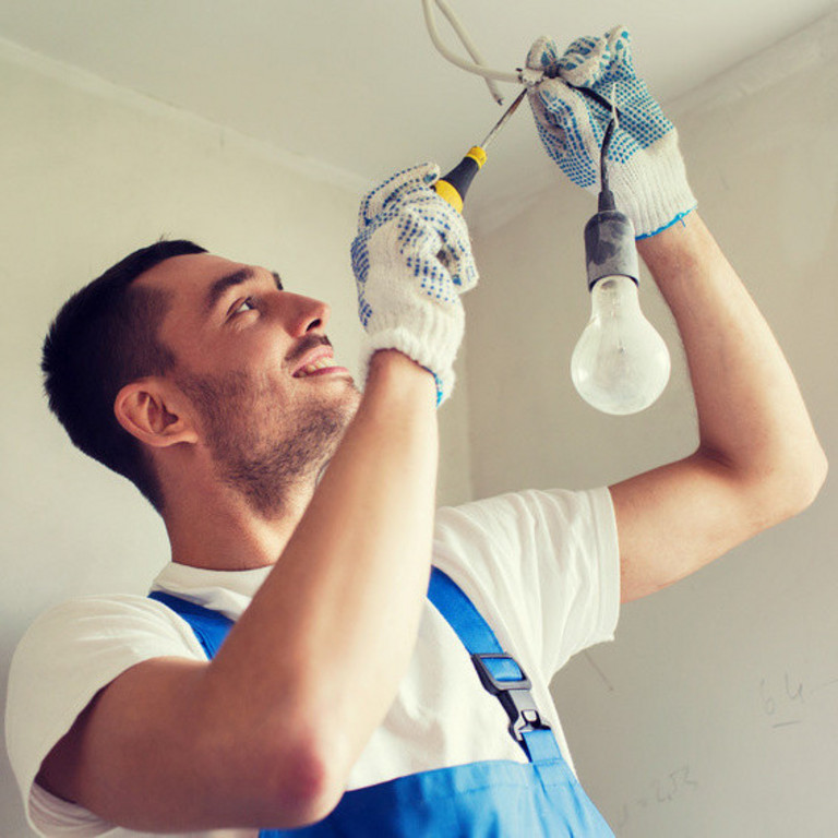 ein Handwerker befestigt eine Glühbirne mit Lüsterklemme unter der Decke