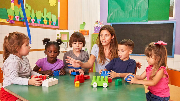 eine Kindergärtnerin sitzt mit Kindern an einem Tisch und spielt