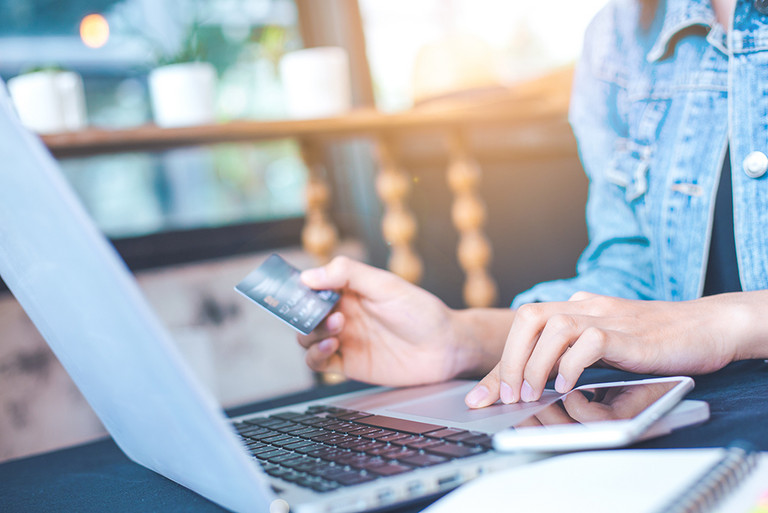 Eine junge Frau hält eine Kreditkarte in der Hand um online zu bezahlen