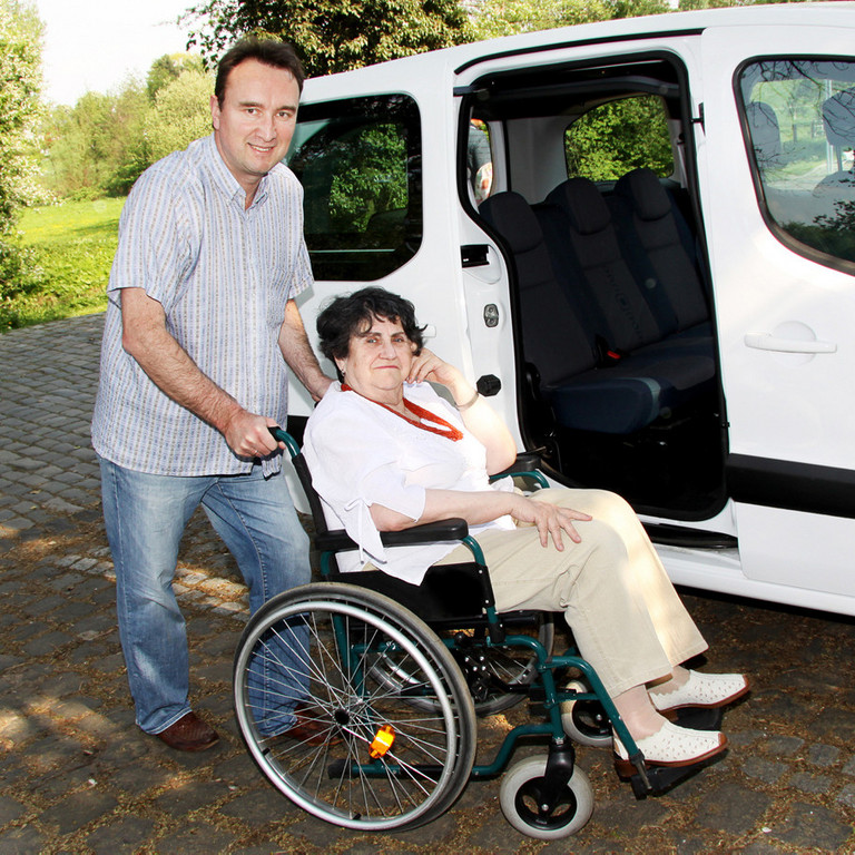 Ein Mann, der eine Frau im Rollstuhl an ein Auto schiebt