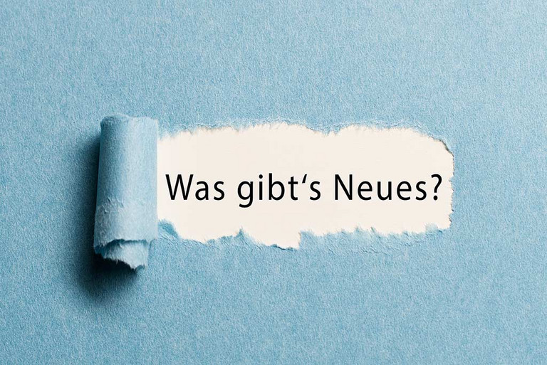 Ein augerissenes Papierstück, hinter dem sich die Frage ''Was gibt`s Neues'' verbirgt