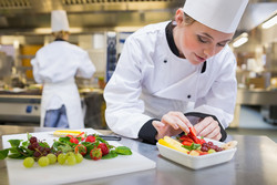 Chefköchin legt eine Erdbeere in den Obstsalat