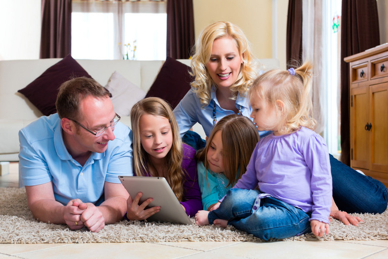 Familie spielt mit einem iPad während sie auf dem Teppich liegen