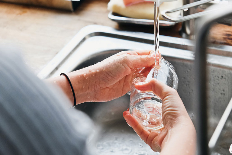 Hände, die ein Glas unter einem Wasserstrahl spülen