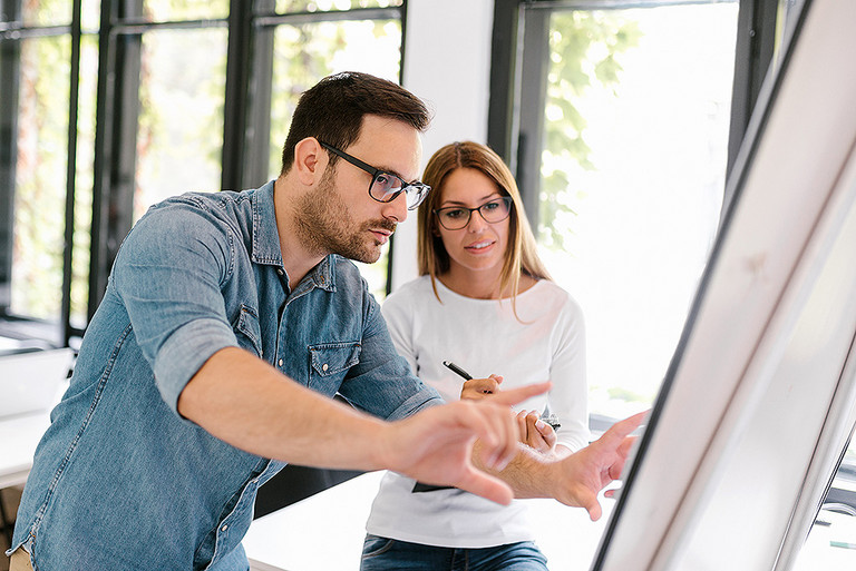 Ein Mann und eine Frau stehen diskutierend vor einem Flipchart