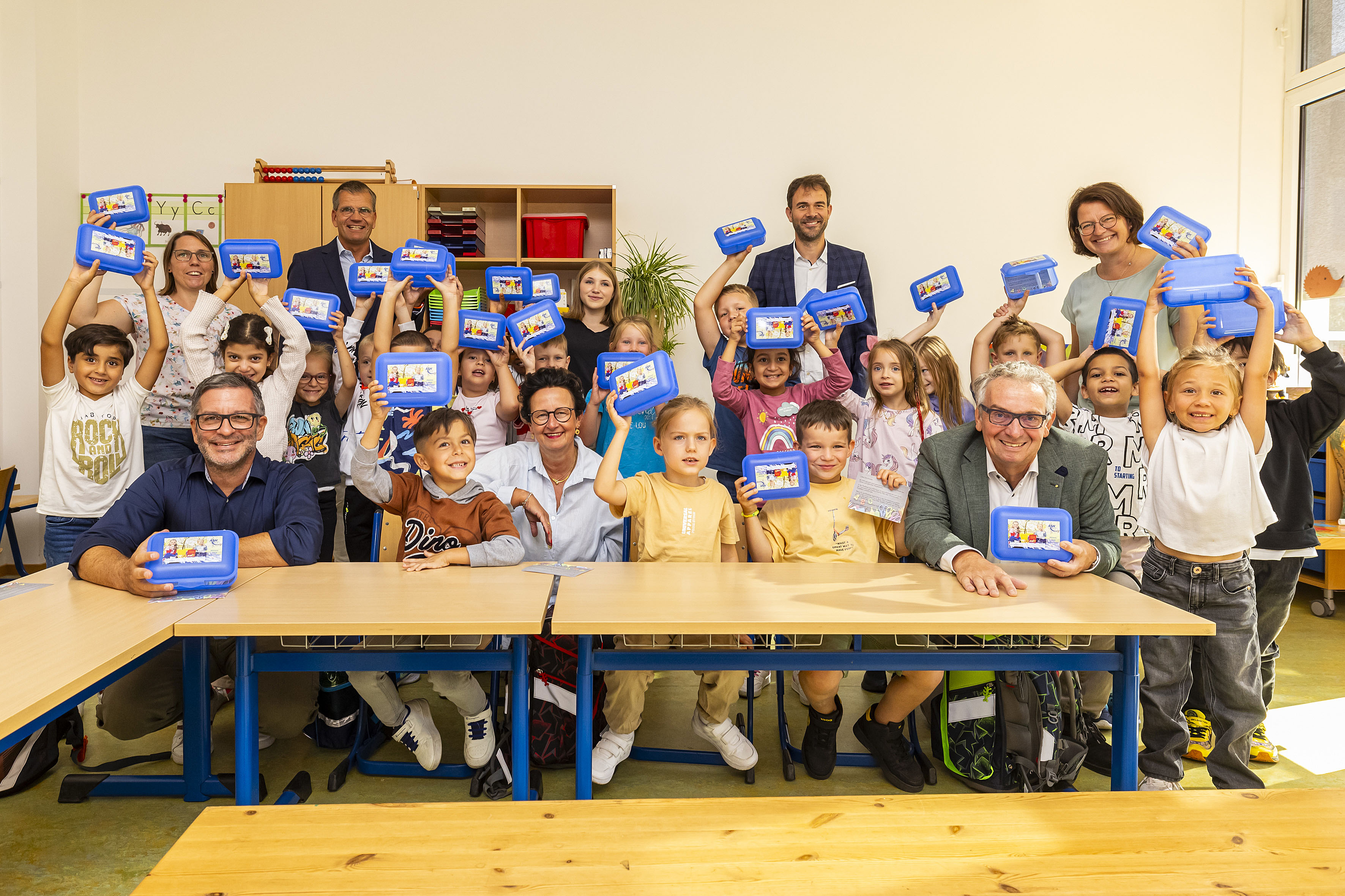 Die Erstklässler:innen der Theodor-Heuss-Schule halten ihre blauen Brotdosen in die Luft.