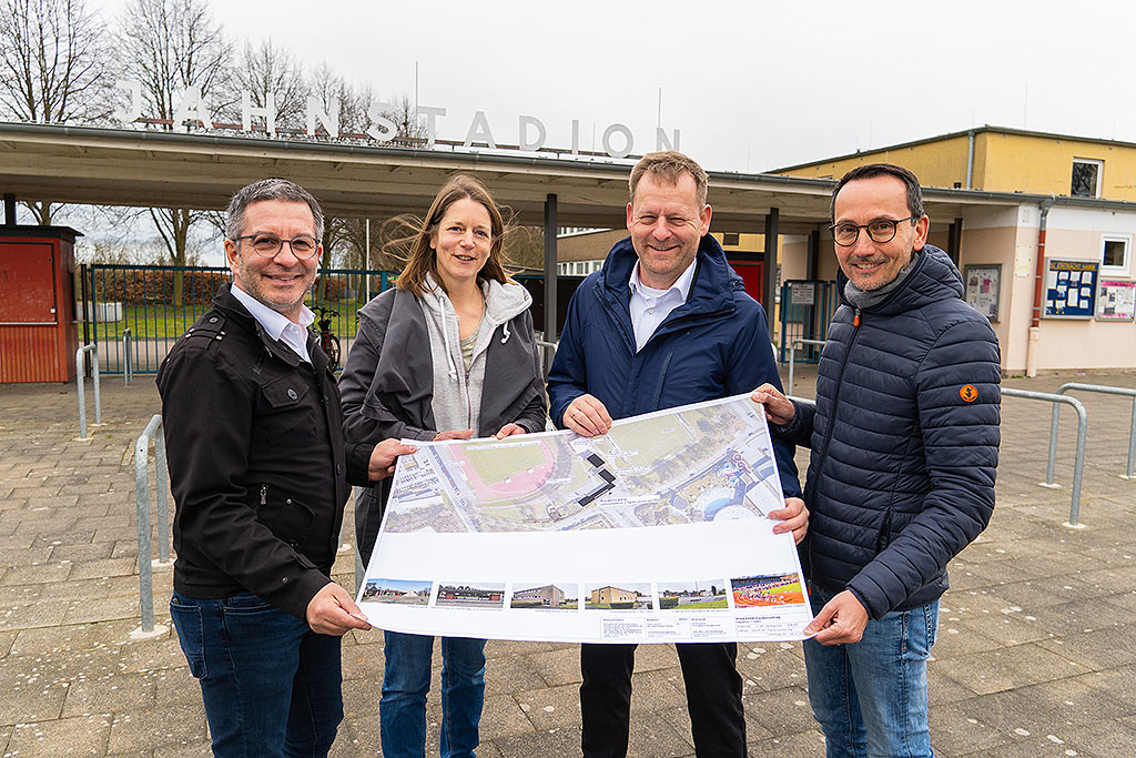 Oberbürgermeister Marc Herter, Heidrun Becker, Stadtbaurat Andreas Mentz und Sportdezernent Markus Kreuz halten einen großen Plan vor dem Jahnstadion.