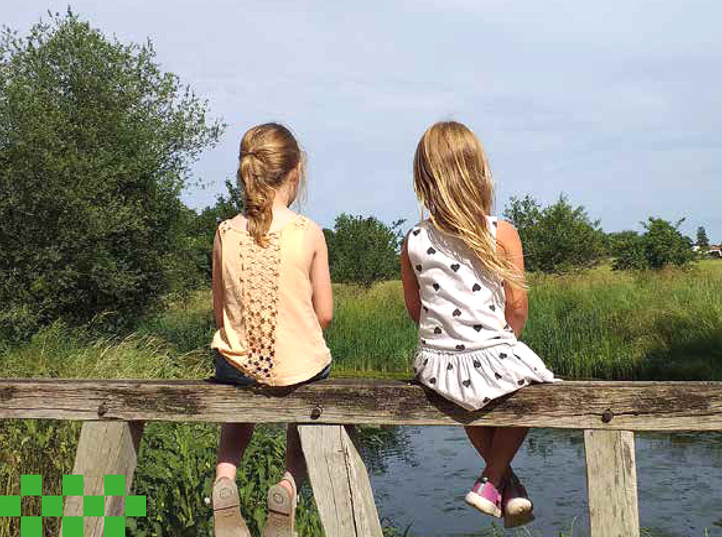 Zwei Mädchen sitzen auf dem Holzgeländer einer Brücke.